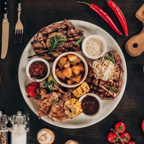 top-view-of-plate-with-beef-steaks-chicken-wings-and-wine-on-table-e1664110794933